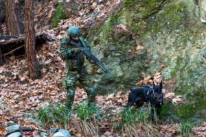 Στρατιωτικός με σκύλο σε δασώδη περιοχή.