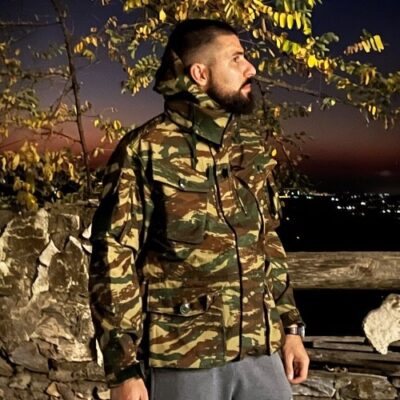 Άνδρας φοράει στρατιωτικό παρκά παρατηρώντας απόγευμα.